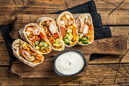 Chicken wrap roll, durum doner kebab with meat and vegetable salad. Wooden background. Top view.