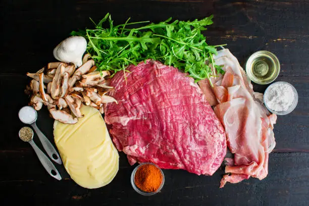 Raw flank steak, mushrooms, cheese, and other ingredients on a wood table