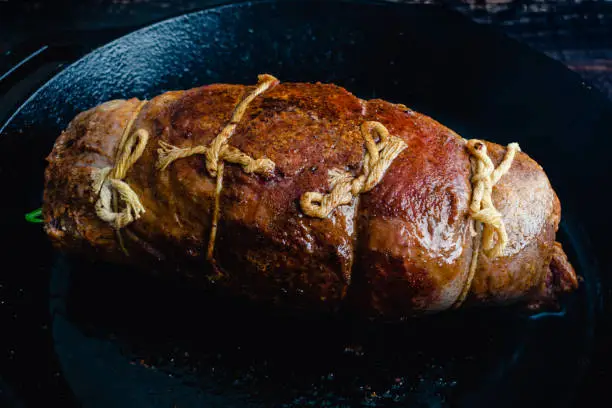 Unsliced steak roulade tied with kitchen string in a cast iron skillet