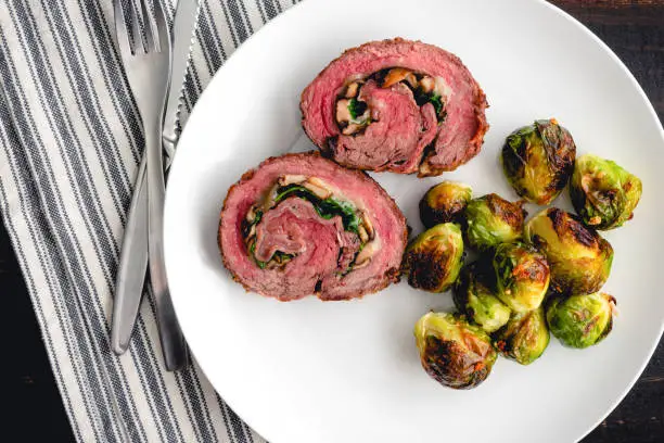 Slices of steak roulade served on a plate with roasted Brussels sprouts