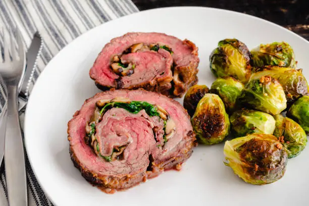 Slices of steak roulade served on a plate with roasted Brussels sprouts