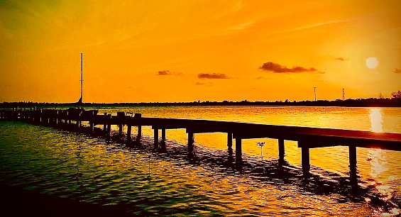 A brilliant sunset begins on Lil Cayman focused on a pier and sailboat