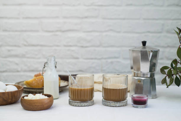 istock Morning table for breakfast. Two glasses of coffee, cottage cheese, eggs, donuts, jam on light table white room. 1467077020
