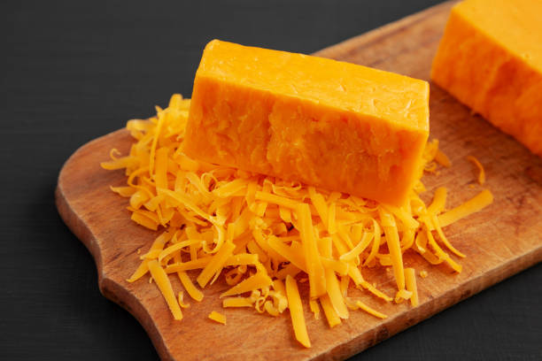 istock Shredded Sharp Cheddar Cheese on a rustic wooden board on a black background, side view. 1467079257