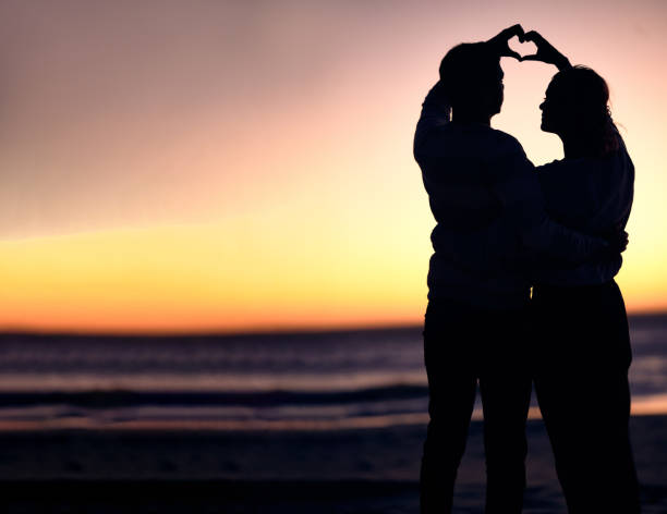 Couple, silhouette and sunset beach with heart shape hands for love, commitment and care on a romantic date, holiday or honeymoon at sea. Man and woman together on ocean vacation for nature travel