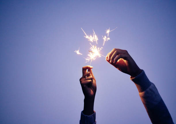 sparkler, mão e pessoa à noite para a celebração da véspera de ano novo com diversão brilhante e ardente para celebrar. celebração, brilho e fundo noturno azul com um fogo-de-artifício ou fogo-de-artifício nas mãos - sparkler sparks new years eve human hand - fotografias e filmes do acervo