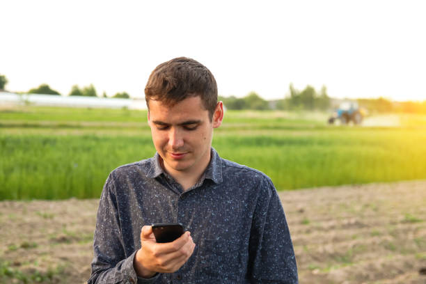 istock Defocus man with phone on sunset. Young farmer working in a wheat field, inspecting and tuning irrigation center pivot sprinkler system on smartphone. Tractor on background. Out of focus 1467086263
