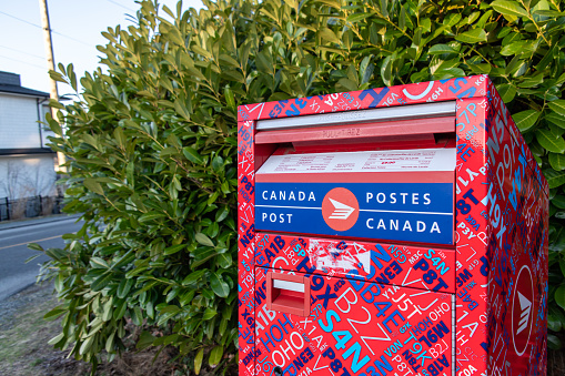 Happy woman in London putting postcard in the mailbox and looking very happy