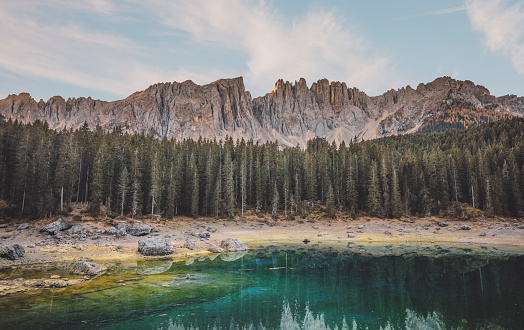 Fantastic nature landscape panoramic view of Mountain lake Lago di Carezza surrounded by pine forest and peaks in early morning in Italian Tirol Alps, Dolomites, Italia
