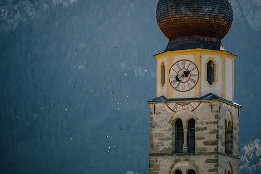 Detail shot of the church bell tower of St. Valentin  Castelrotto Kastelruth Village Church on a sunny spring day against flying birds and  Schlern mountains of the Italian Alps, Alto Adige, Italia