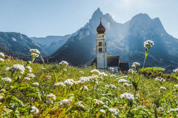 Fall landscape view of St. Valentin  Castelrotto Kastelruth Village Church on a sunny spring day with white flowers in the middle of a green valley surrounded by the Schlern mountains of the Italian Alps, Alto Adige, Italia