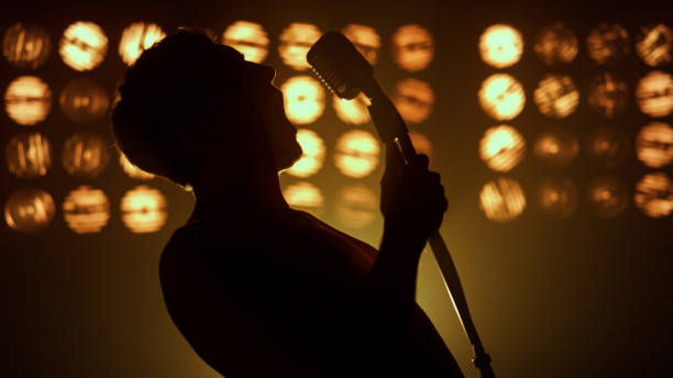 Professional singer performing song firely on stage nightclub close up. Silhouette unknown man performer raising mic on scene lights. Emotional guy vocalist singing microphone solo on show party.
