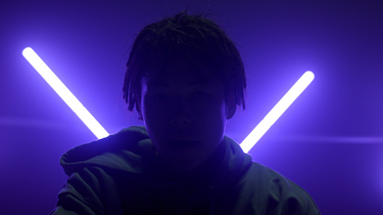 Silhouette man posing in dancing studio illuminated ultraviolet lamps. Unknown young guy wiping face standing stage in blue led lights close up. Portrait stylish b-boy with dreadlocks in nightclub.