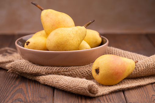 Fresh ripe pears in a basket on a brown wooden table with a place for inscription