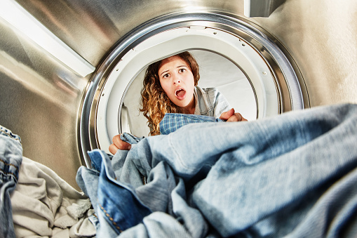 Attractive young woman with curly hair gasps open-mouthed as she checks out her newly dried clothes. Unusual angle from inside the appliance itself.