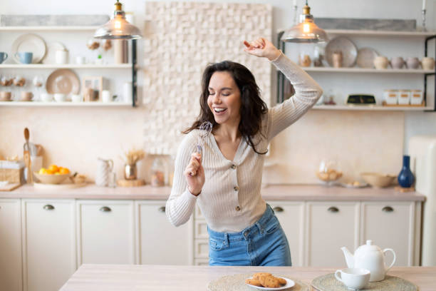 istock Playful woman singing at appliance as imaginary microphone, dancing in kitchen interior alone, free space 1467118937