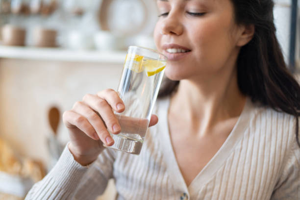 istock Refreshment concept. Young woman drinking water with lemon, holding glass, standing in kitchen, closeup 1467118974