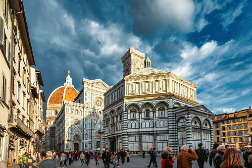 People walk on Piazza del Duomo, beside Florence Cathedral, in downtown Florence, Tuscany, Italy at sunset. The cathedral complex is a UNESCO World Heritage Site.