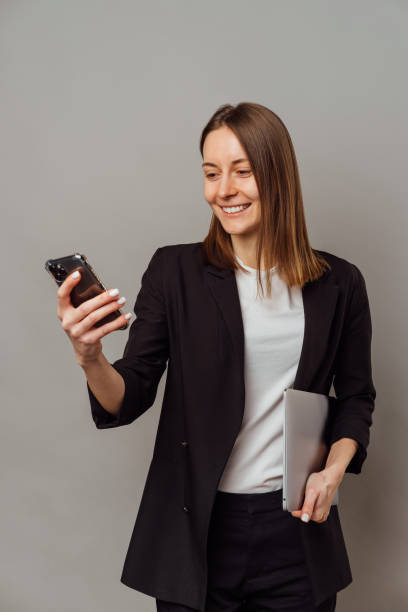 Smart smiling woman wearing jacket is holding a laptop and her cellphone. stock photo