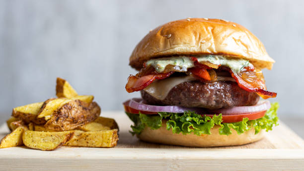 Spectacular burger with onion, bacon, fresh lettuce with sweet bun and fries on the side Traditional American sandwiches pork, grilled, beef sesame photos stock pictures, royalty-free photos & images