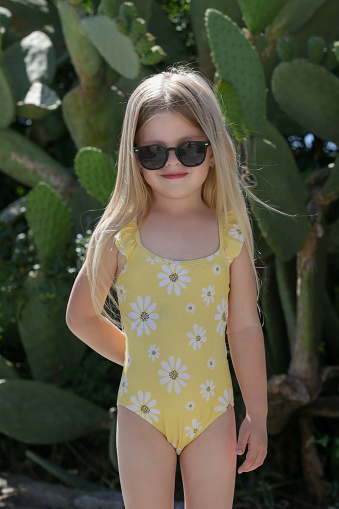 Adorable five years old girl in yellow swimsuit and black glasses on summer vacation, candid outdoor portrait in park