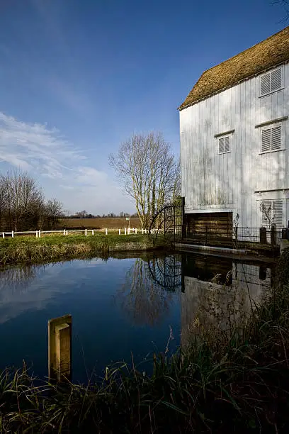 English watermill bathed in winter sunlight reflecting in the calm millpond with striking blue sky
