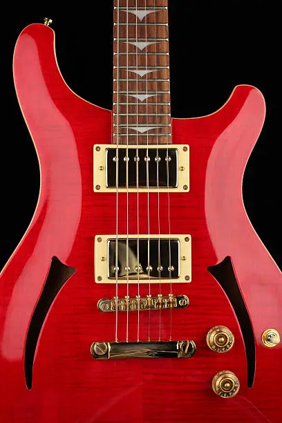 Beautiful close up of a flamed maple, cherry red, semi-hollow body electric guitar isolated on black background.