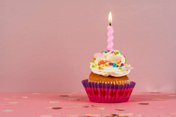 istock Birthday cupcake with candle light on a pink background. Cake with whyte cream and confectionery decor. Festive dessert and congratulations. Happy Birthday. 1467163942