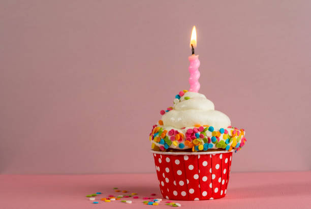 istock Birthday cupcake with candle light on a pink background. Cake with whyte cream and confectionery decor. Festive dessert and congratulations. Happy Birthday. 1467163949