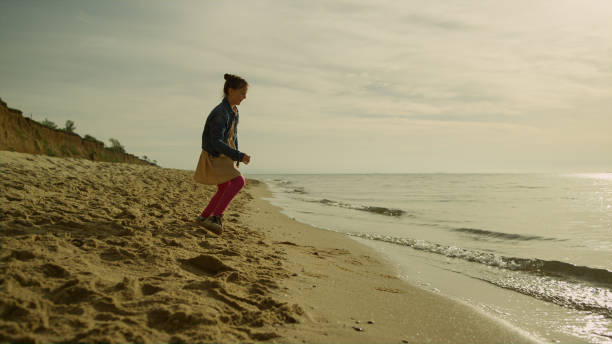 istock Small girl playing outdoors on sunset beach. Happy kid relaxing alone at seaside 1467169958