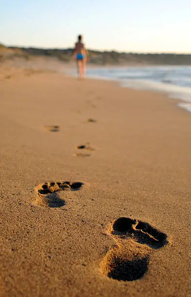 Lone woman out of focus walking on beach with two footsteps in foreground