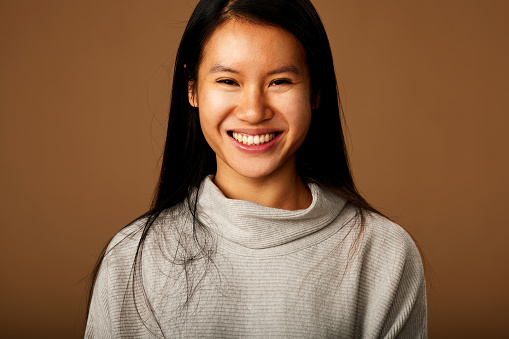 Head shot of a happy asian girl smiling at the camera while posing in studio.