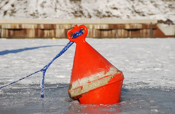 A small red buoy icebound in winter