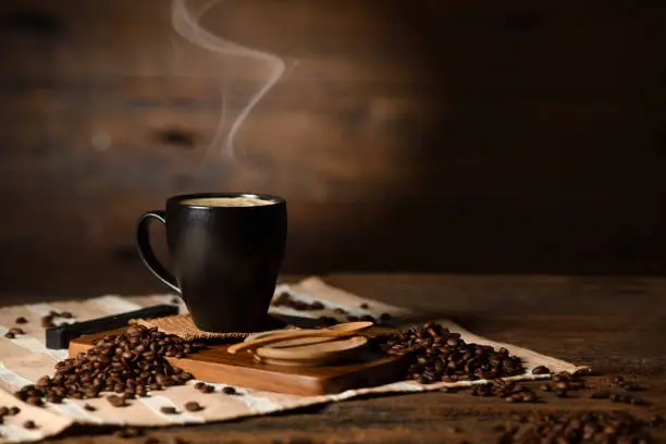 Photo of Cup of coffee with smoke and coffee beans on old wooden background