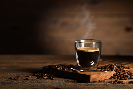 Cup of espresso with coffee beans, bag, scoop and steam on rustic wooden background