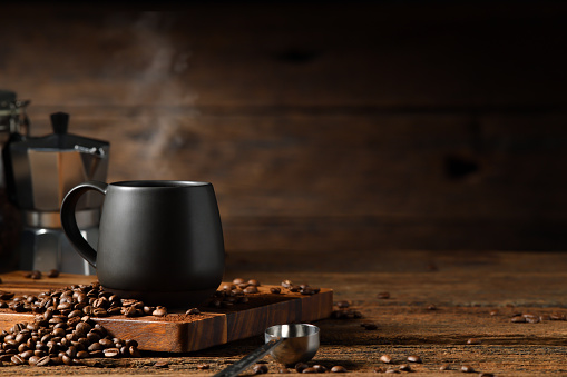 Cup of coffee with smoke and coffee beans on old wooden background. Moka pot and coffee cup. Moka pot and coffee cup