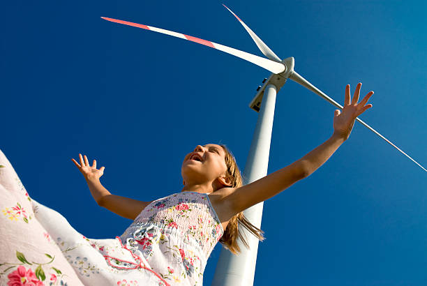 Smiling girl with arms outstretched below a windmill stock photo