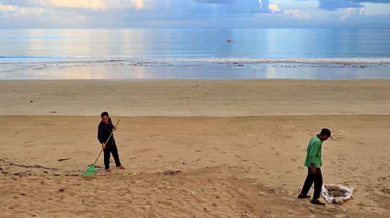 Low section of man cleaning seaweed on a sandy beach. Pollution problem rises with climate . Copy space