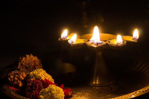 panch pradeep or five headed oil lamp burning with glowing flame with marigold flowers. these are used in hindu puja rituals like durga , saraswati , kali , laxmi puja, shivaratri, holi or diwali.