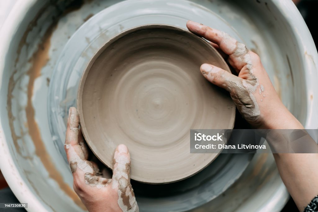 Top view of potter's wheel with ceramic plate and hands Hands of young woman master of ceramics working on a potter's wheel, making plate of clay in own art studio. Close up, top view Pottery Wheel Stock Photo