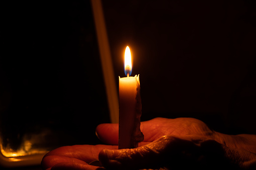 old woman's hands and candle flame in the dark, candle light, mourning, candle in the dark