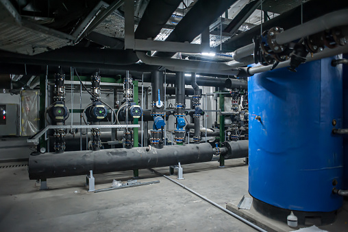 Huge industrial boiler services and air handling unit in the ventilation plant room with ductworks and insulated pipelines