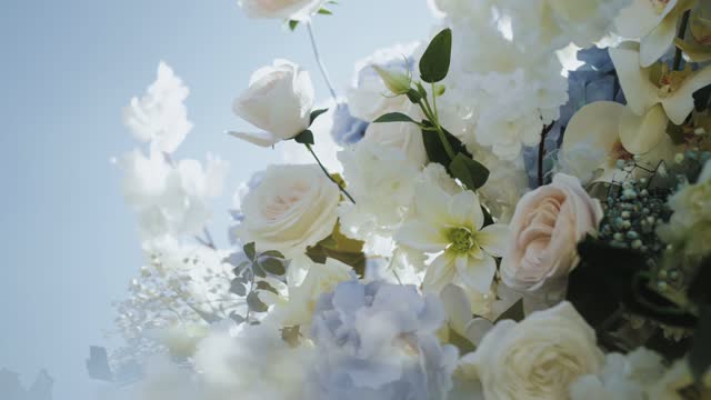 Close-up of wedding arch decorated with flowers in white and blue colors, roses, chrysanthemums and hydrangeas, blue sky on the background slow motion, outside wedding ceremony.