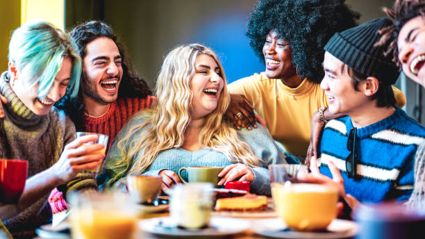 Friends group laughing together at coffee bar - Young people talking and having fun at cappuccino restaurant - Life style concept with diverse guys and girls at cafe breakfast venue - Vivid filter stock photo