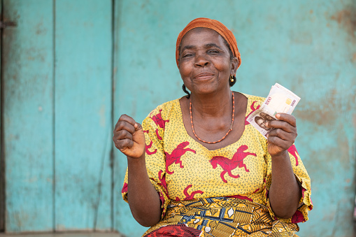 An elderly African woman outdoors holding money