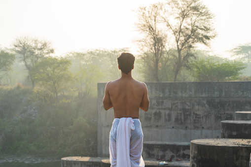 The young Indian priest praying to the sun early in the morning while wearing a dhoti.
