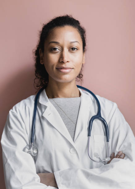 Portrait of a young female doctor standing against brown wall stock photo