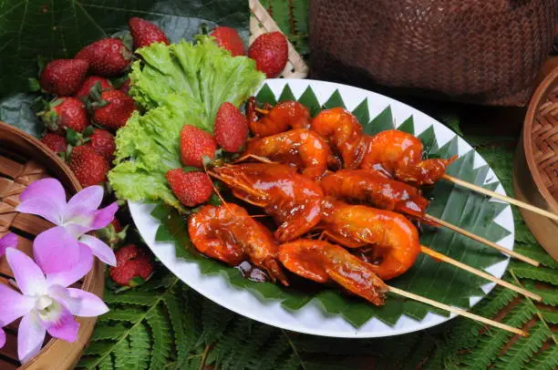 Photo of Top view of a plate of Caridean Shrimp on sticks next to strawberries