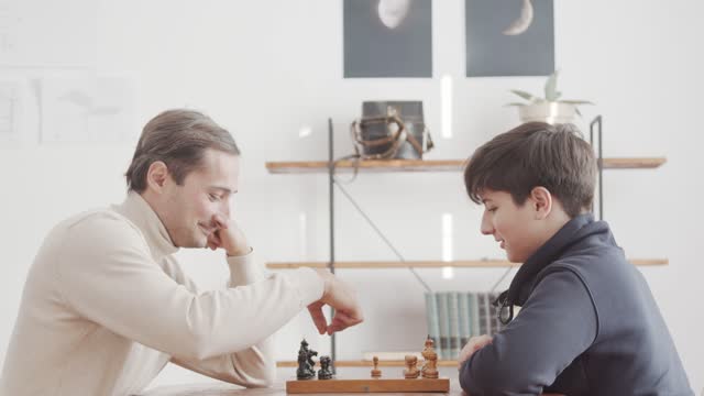 A father and a teenager son communicate while playing chess. Showing interest and intelligence. Family pastime. Proper education of the next generation