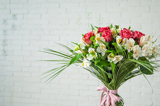 A beautiful bouquet with roses and white alstroemeria against a white wall